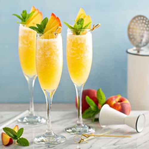 Peach Bellini served in a champagne flute with fresh peach slices and mint garnish.