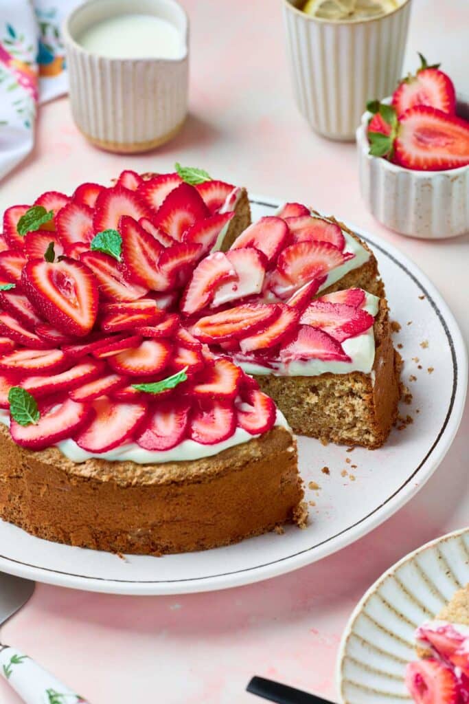 Strawberry meringue cake cut up and topped with ripe thinly sliced strawberries