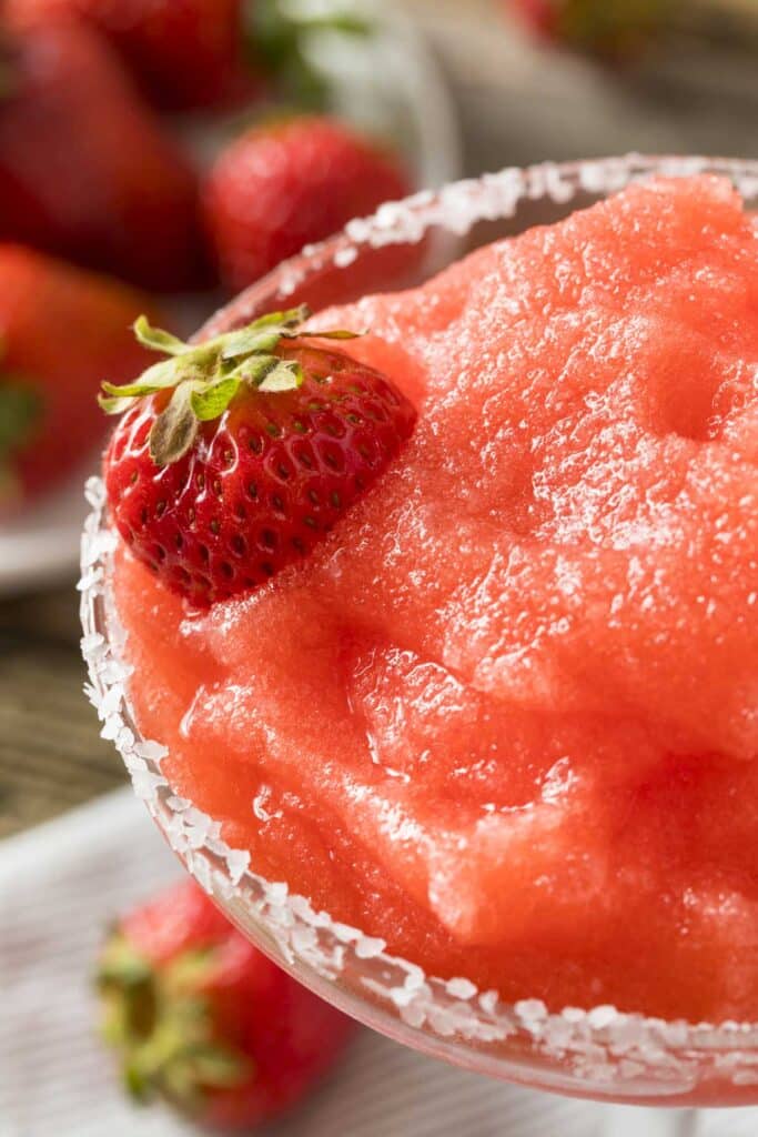 Close up view of salt-rimmed glass with frozen strawberry margarita and garnished with a strawberry