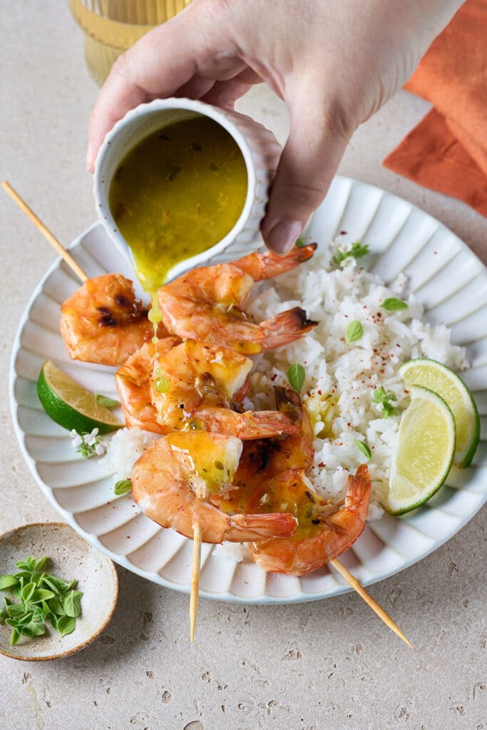 Mojo sauce getting poured over shrimp skewers and rice