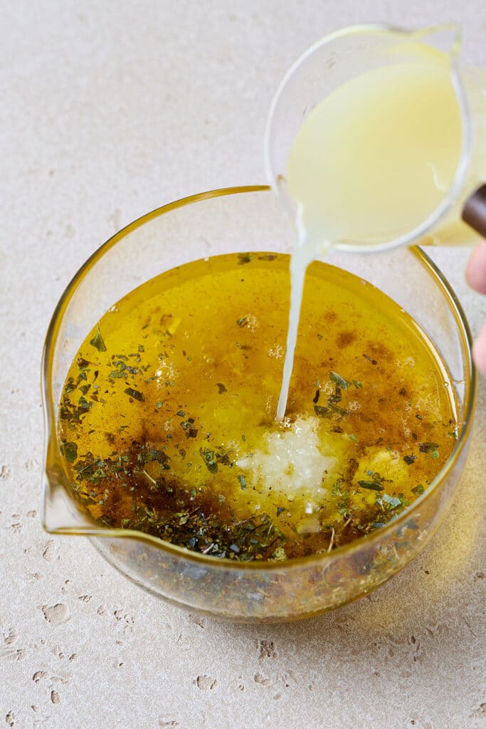 Adding lemon juice to a container with herbs, grlic and oil