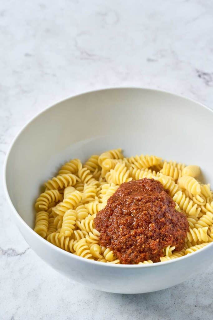 A bowl of cooked short pasta topped with sundried tomato vinaigrette