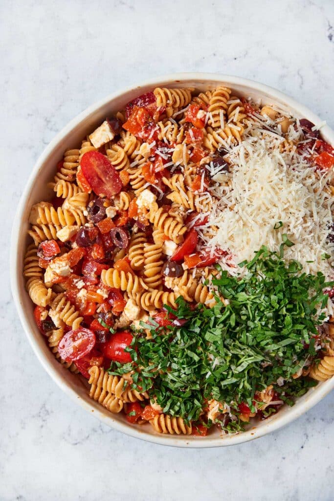 A bowl with tossed Mediterranean pasta salad with sundried tomatoes topped with fresh basil, parsley and shredded Parmesan cheese