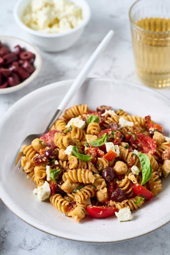 A plate with a Mediterranean style pasta salad with sun-dried tomatoes, olives, Parmesan and chickpeas