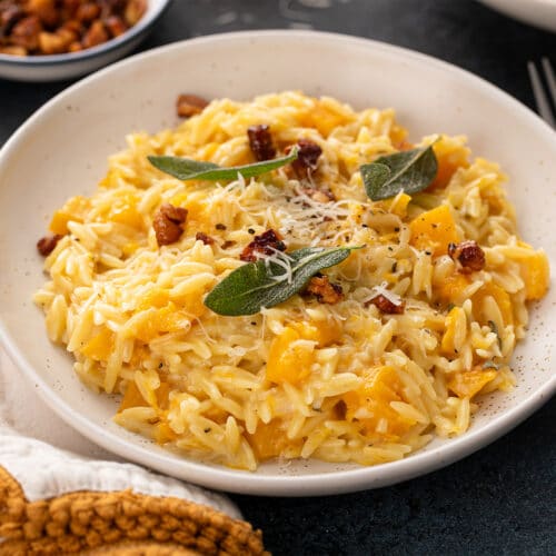 Bowl of creamy butternut squash orzo topped with sage, Parmesan and candied pecans.