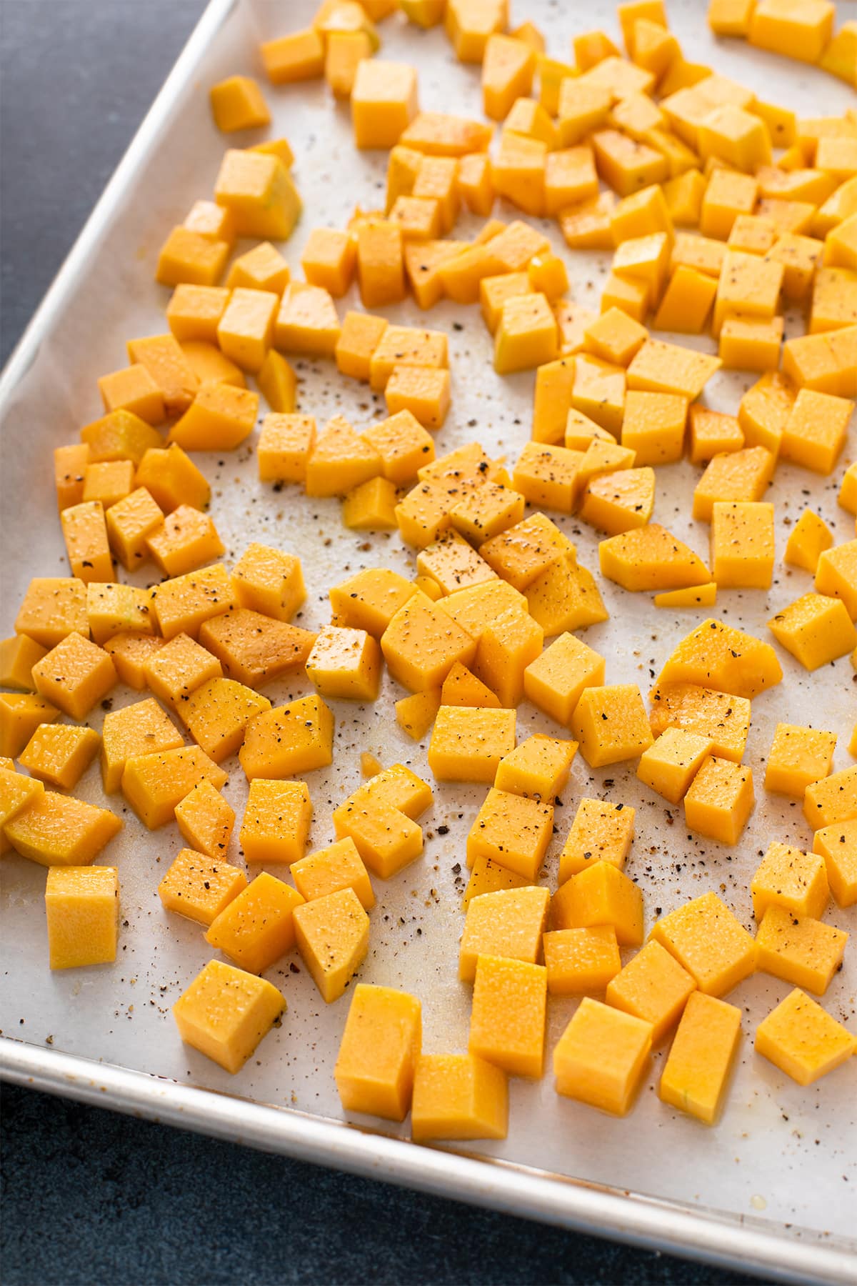 Cubed butternut squash seasoned with salt and pepper on a parchment-lined sheet pan.