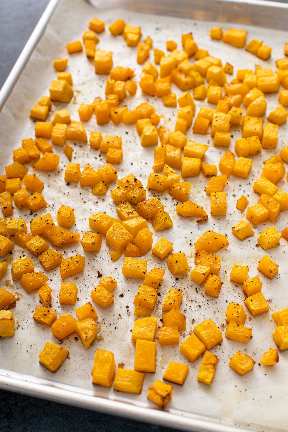 Roasted butternut squash cubes with golden brown edges on a sheet pan.
