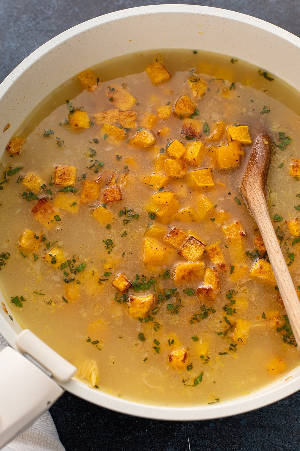 Roasted butternut squash and broth added to toasted orzo in a skillet.