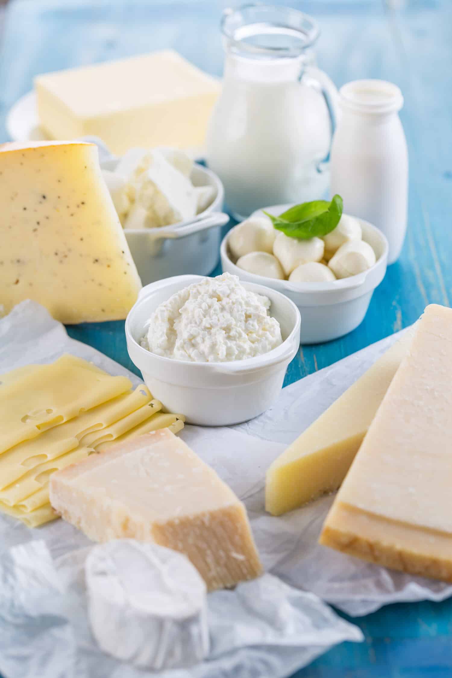 Assorted cheeses on a board beside a bottle and glass of milk.
