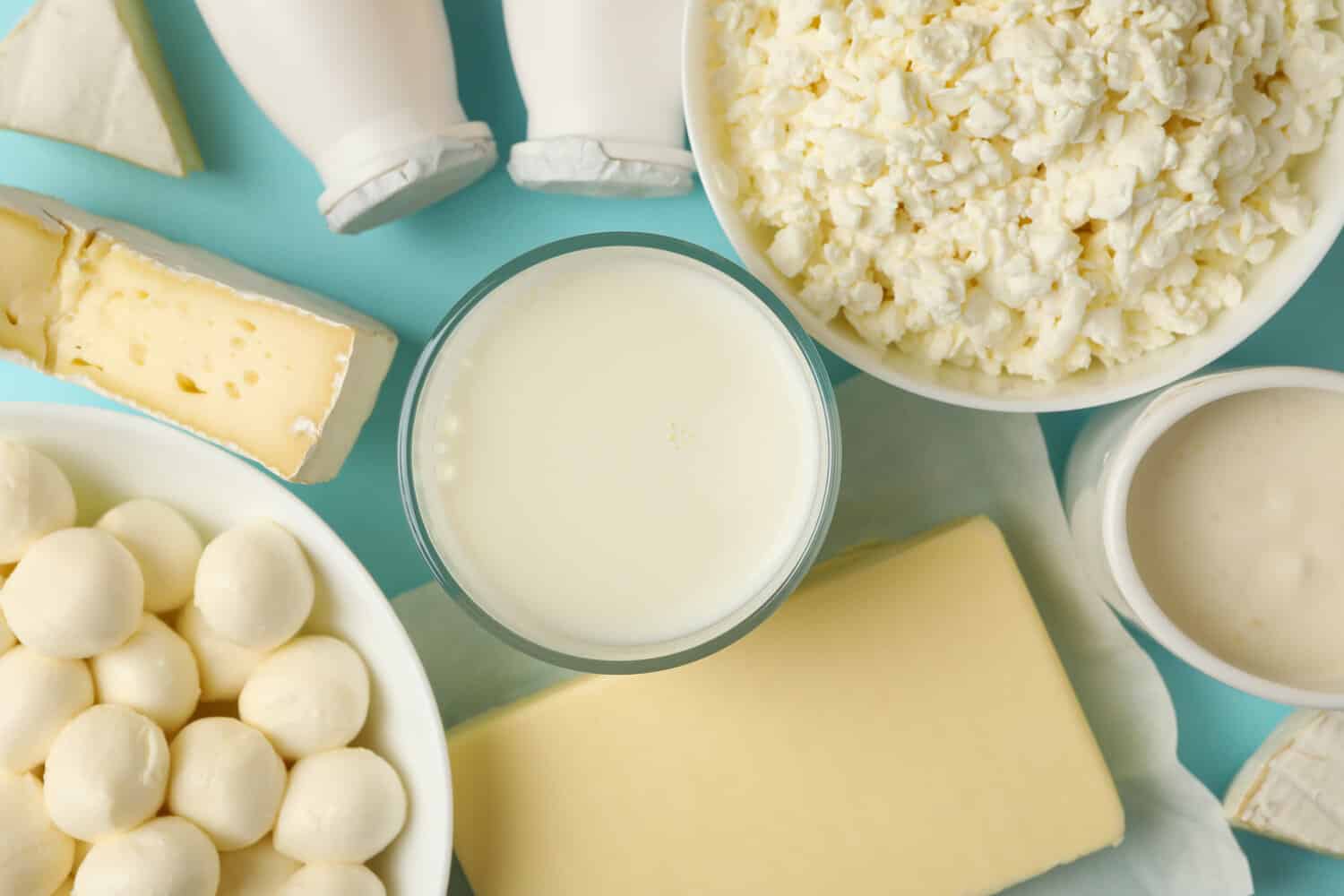 Overhead view of milk, cottage cheese, mozzarella balls, butter and soft cheeses on a blue background.
