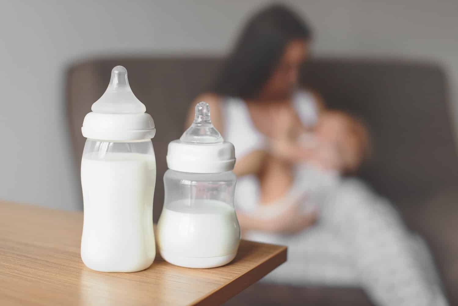 A mother holding a baby bottle of milk while feeding her infant.