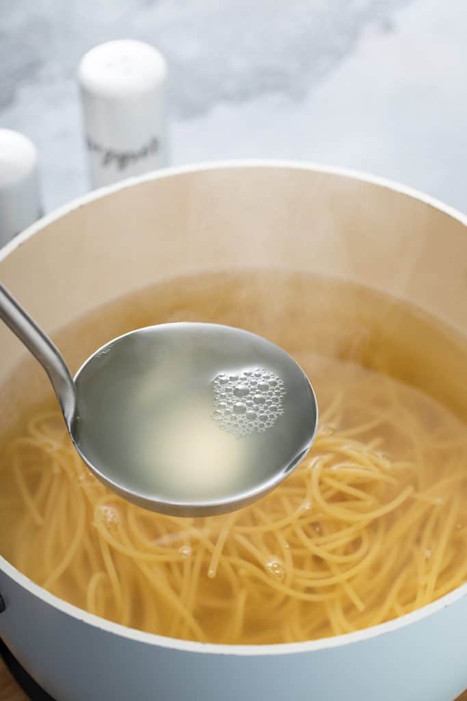 A ladle scooping starchy cooking water from a pot of spaghetti.