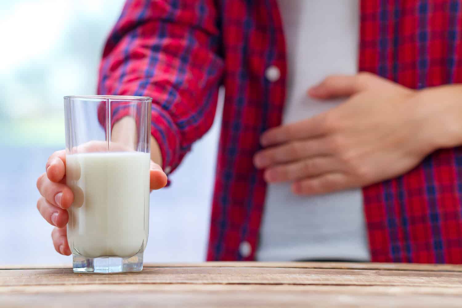 A person holding a glass of milk with their other hand on their stomach.