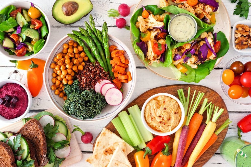 A table spread with salads, roasted chickpeas, hummus, fresh vegetables and pita.