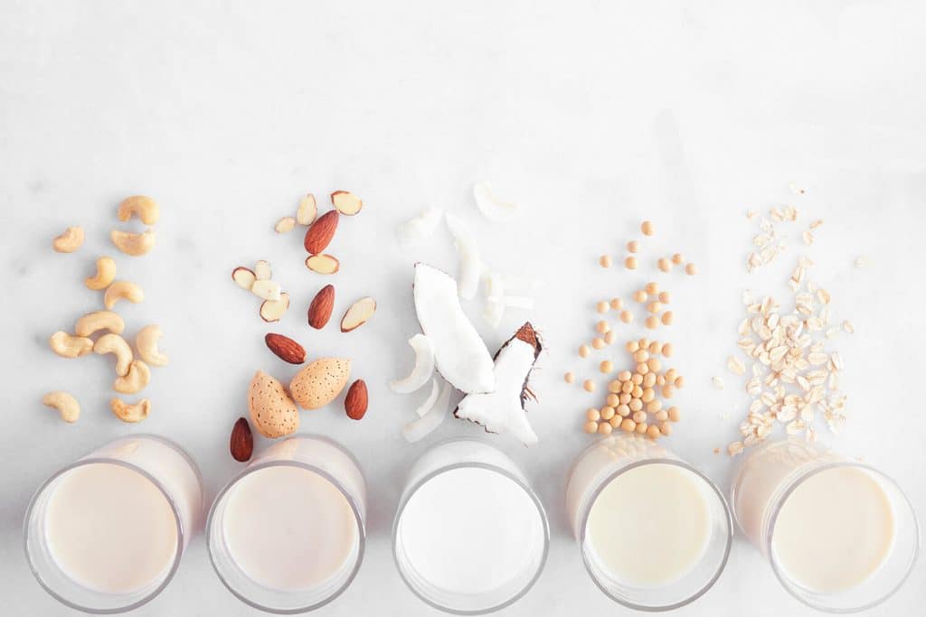 Five glasses of plant milk, each with its source above it: cashews, almonds, coconut, soybeans and oats.