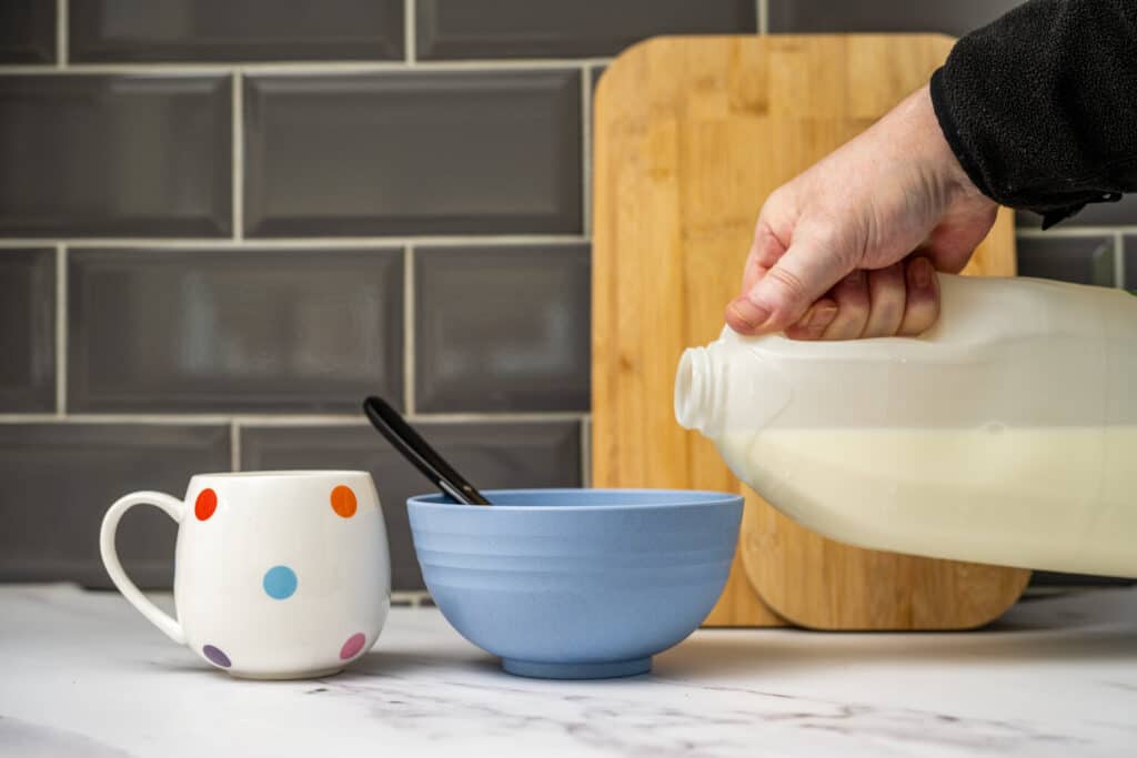Milk being poured from a gallon jug into a bowl of cereal.