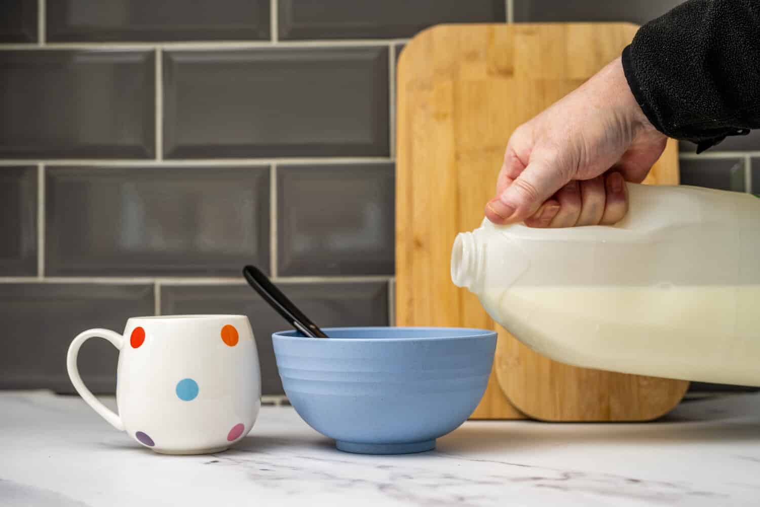 Milk being poured from a gallon jug into a bowl of cereal.