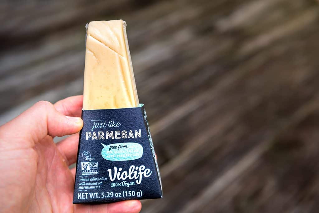 A hand holding a wedge of Violife plant-based parmesan.